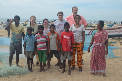 Students posing with some local children and their parents on the beach