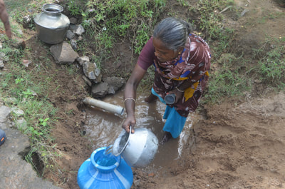 An Indian women collecting water after sawing through a pipe.